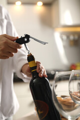 Woman opening wine bottle with corkscrew at table indoors, closeup