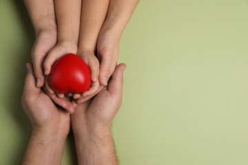 Parents and child holding red decorative heart on light green background, top view. Space for text