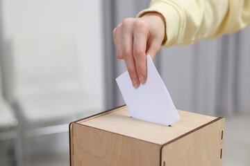 Woman putting her vote into ballot box on blurred background, closeup