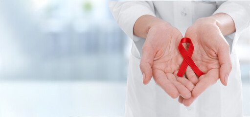 Cancer awareness. Doctor holding red ribbon on blurred background, closeup. Banner design with space for text