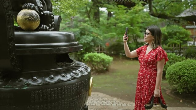 Hispanic woman in glasses captures japan's ancient gotokuji temple beauty with her phone, enjoying her role as a tourist