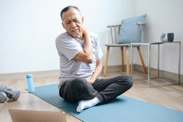 Senior Asian man suffering from stiff shoulders while having training exercise at home