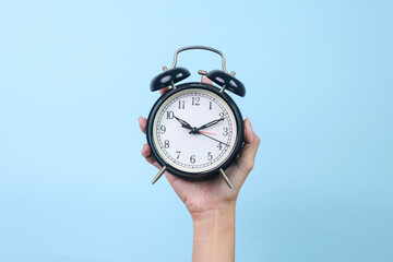Hand holding classic black alarm clock against blue background