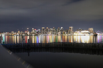 View of the night scene of downtown in the evening, yachts drift peacefully on the water's surface. Framed by city buildings, with distant lights adding to the urban ambiance. Cityscape at night.