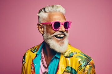 Portrait of a cheerful senior man in sunglasses and a colorful shirt on a pink background.
