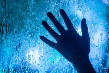 A hand is shown through a window with raindrops on the glass