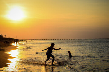 silhouette of a children play in water on the beach at sunset