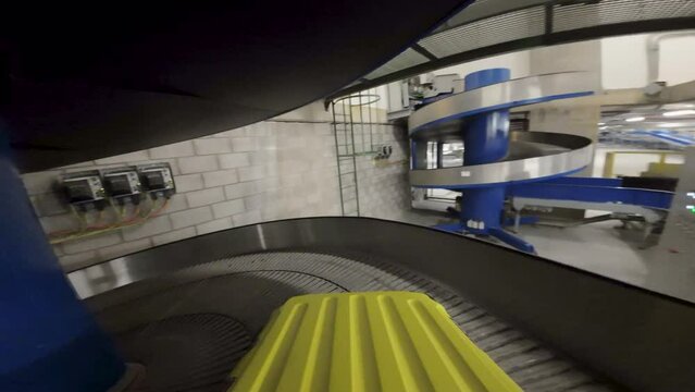Yellow suitcase on conveyor belt in airport baggage area, about to be loaded onto plane, industrial setting