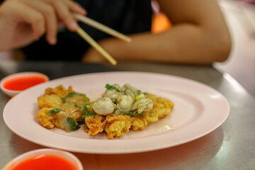 Person eating thai omelette with oyster and greens 