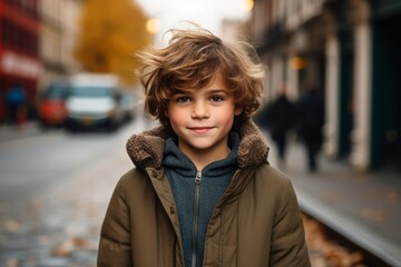 Outdoor portrait of cute little boy with blond curly hair, wearing warm clothes, posing on the street.