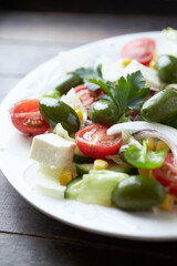 Salad with Feta Cheese, Green Olives, Baby Spinach, Cucumber, Cherry Tomatoes and Capers. Dark wooden background. Close up.	