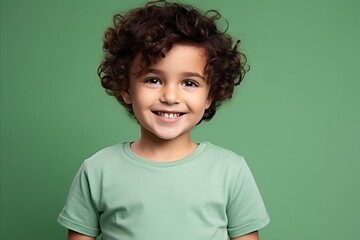 Portrait of a cute little boy with curly hair against green background