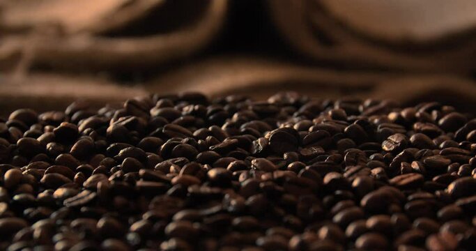 Close up static shot of dark brown, freshly roasted coffee beans. Close-up focus shot of fresh coffee beans with linen sack in blurred background.