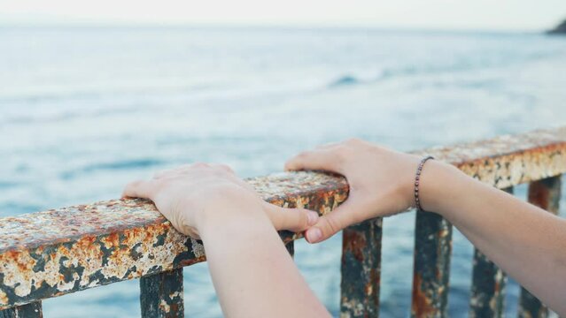 Female putting hands on rusted metal railing on waterfront, depression concept