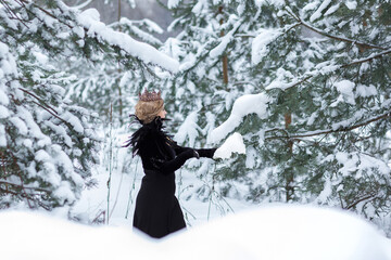 Fototapeta na wymiar Fashion concept. A beautiful young lady with blond hair and a long black dress, with a crown on her head, stands in a winter park. Beautiful dark princess using a black magic spell.