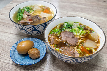Two bowls of Taiwanese beef noodle soup, an egg and a meatball on rustic wooden table, showcasing a delicious and comforting meal made with fresh ingredients