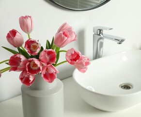 Vase with beautiful pink tulips and toiletries near sink in bathroom, closeup