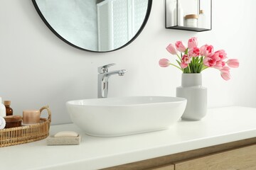 Vase with beautiful pink tulips and toiletries near sink in bathroom