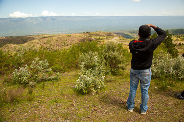 An individual stands on a hilltop, contemplating the expansive landscape and mountain range before...
