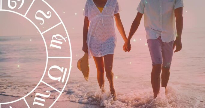 Animation of horoscope moving over biracial couple holding hands at beach