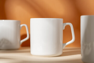 White ceramic mugs on peach background with shadows