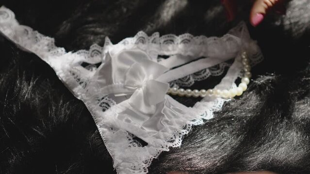 White lace lingerie with pearls placed by a woman's hand. The image has a sensual and intimate atmosphere.