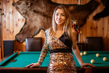 A woman in gold and black dress stands in front of a pool table