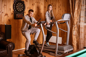 Fototapeta na wymiar A man and woman are exercising on stationary bike in living room