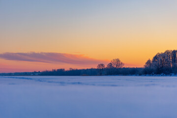 Fototapeta premium A beautiful winter sunrise scenery of frozen lake and forest. Colorful landscape with dawn skies in Northern Europe.