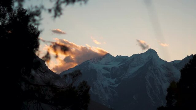 4K shot of orange clouds above the snow covered Himalayan mountain during the sunset as seen from Tayul Monastery near Keylong in Lahaul Valley, Himachal Pradesh, India. Sunset background.