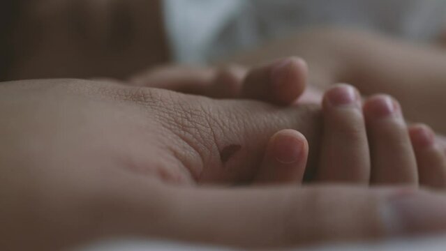 A toddler holding father hand during baby sleeping. Father taking care of her son kid happy family dream of health