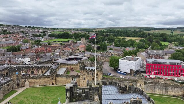 Alnwick, England UK. Aerial View of British Flag Waving on Castle Tower and Cityscape, Orbiting Drone Shot 60fps