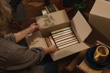 Relocation, movement. Young woman packing books in moving box.