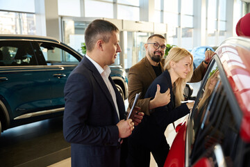 Three people are standing in a car dealership