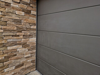 Modern gray brown, beige, metal door at the house lined with stone cladding. gutter for drainage of...