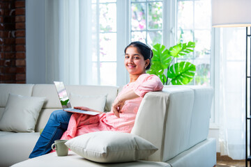 Indian young female with a laptop sitting sofa in a modern living room