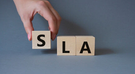 SLA - Service Level Agreement. Wooden cubes with word SLA. Businessman hand. Beautiful grey...