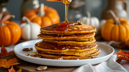 A woman carefully pours honey onto a plate of pumpkin pancakes, adding a sweet touch to the warm, spiced breakfast dish.