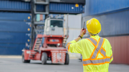 Asian foreman in hardhat and safety vest talking on the walkie-talkie control loading Containers box at warehouse logistic in Cargo freight ship for import export in harbor, shipping loading in docks