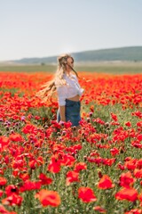 Happy woman in a poppy field in a white shirt and denim skirt with a wreath of poppies on her head posing and enjoying the poppy field.