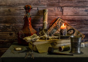On the table are antique nautical maps, a box, a leather-wrapped bottle and a metal goblet, a smoking pipe and a pocket watch. Burning candle.