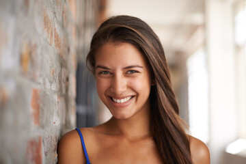 Portrait, smile and woman by brick wall at school for confidence, education or learning in corridor...