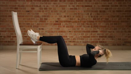 A fitness expert instructs on elevated feet crunches using a chair, intensifying core strengthening and advancing abdominal conditioning in a minimalist gym environment. Camera 8K RAW. 