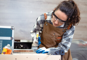 Female latino carpenter using tool busy working her job in furniture renovation small business. Hispanic woman wear goggles standing in DIY carpentry workshop. Empowerment joiner women in woodworking.