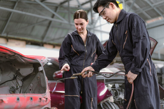 Skilled welder welding damage auto body car with blue spark at workshop. Auto mechanic in uniform working at repair garage station fixing broken vehicle. Repairman occupation in automotive maintenance