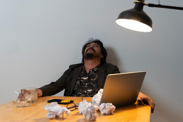 Asian businessman fails, man in despair drinks hard liquor, sitting late at the table in the office.