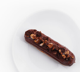 eclair with chocolate and nuts on a white plate