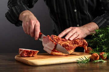 The cook cuts smoked pork on the kitchen table. - obrazy, fototapety, plakaty
