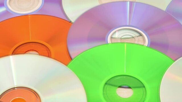 Pile of multicolored CDs and DVDs on the table. Tracking shot. Vintage technology concept. 