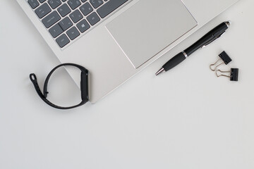 Close up of a silver laptop with a black pen and a black smartwatch on an office desk.
